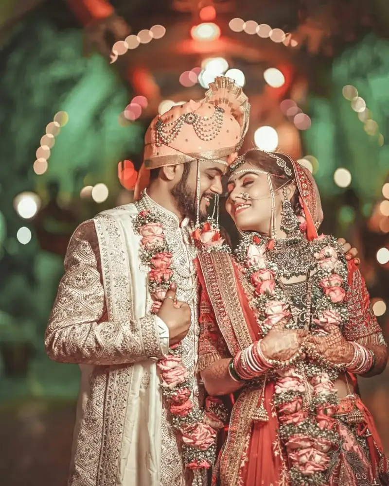 Bride and groom in flower garlands under strings of lights.