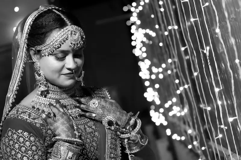 Black and white portrait of a bride beside a curtain of fairy lights.