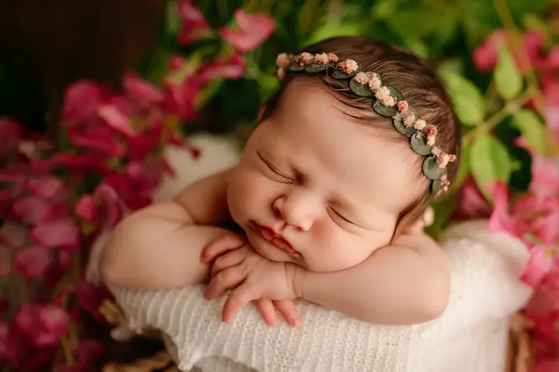 Newborn baby asleep in a wrap, surrounded by pink flowers.