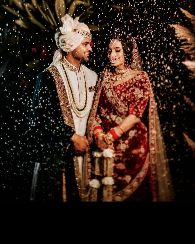 Bride and groom together at night as flower petals fall around them.