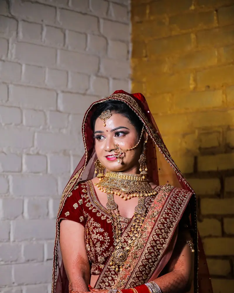 Bride in a red lehenga photographed against a white brick wall at Dream Studio.